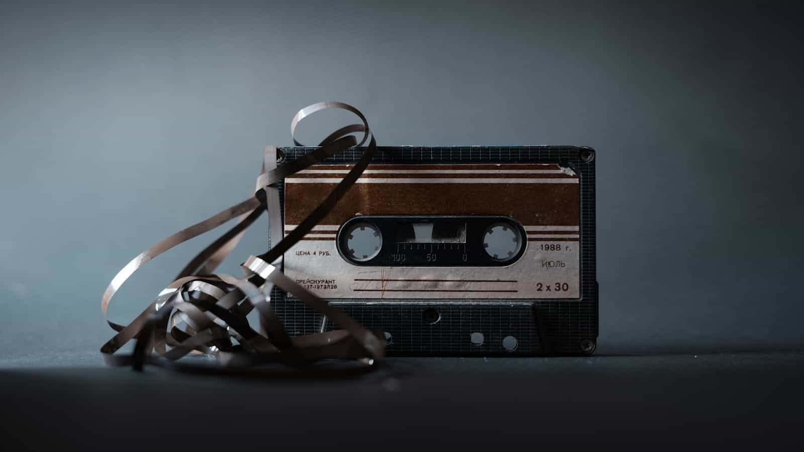 Retro audio cassette with tape out placed on gray surface and illuminated by light in studio